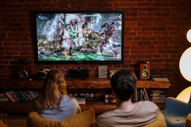 CDKeys gaming banner showing the back of a man and woman sitting on a sofa playing a game on a wall mounted tv