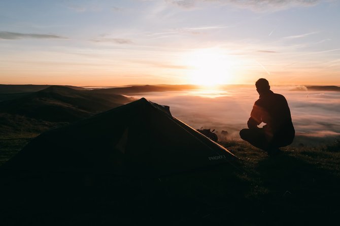Guy camping by the sunset in the mountains