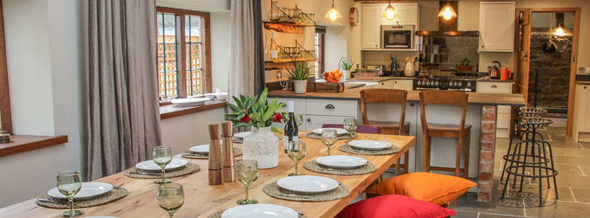 Sky Cottages discount code banner - dining table and kitchen area in a cottage, set up with glasses and plates
